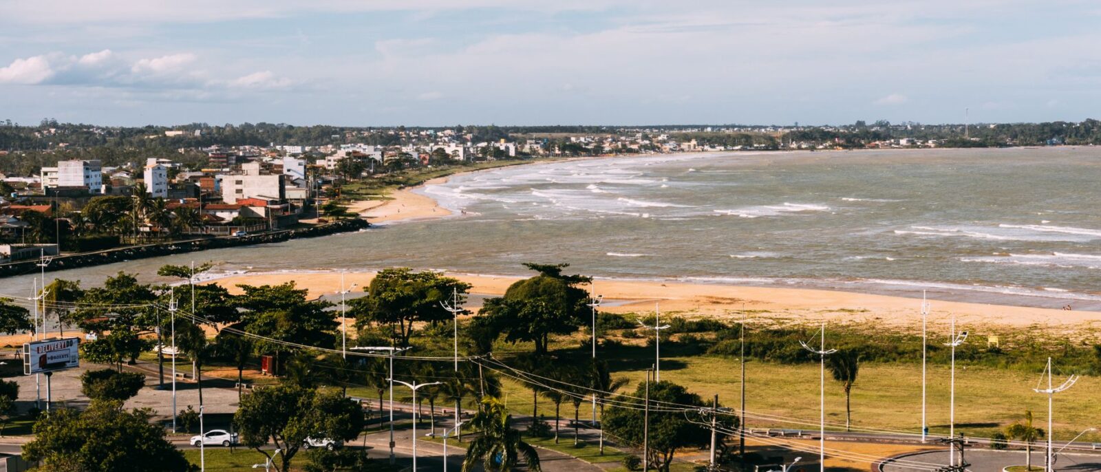 Vista aérea de uma cidade costeira com praia, oceano e edifícios modernos em um dia ensolarado